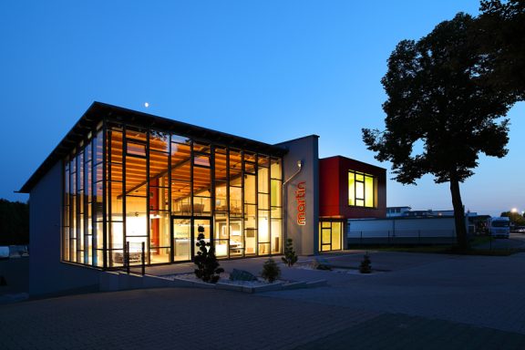 Moderne Architektur mit Glasfront und heller Beleuchtung bei Dämmerung.